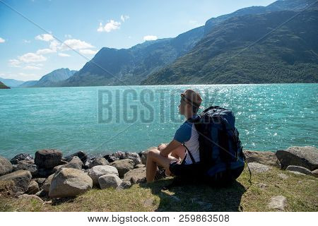 Hiker With Backpack Resting Near Gjende Lake In Jotunheimen National Park, Norway