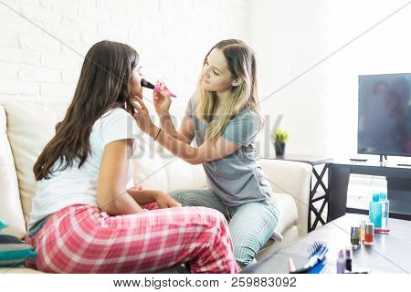 Woman Using Make-up Brush On Friend's Face At Home