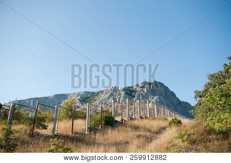Long High Fence With Barbed Razor Wire Near Rocky Mountains In Mexico Usa Border Outdoors