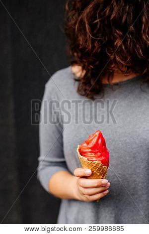 Red Ice Cream In The Hand Near Black Wall.