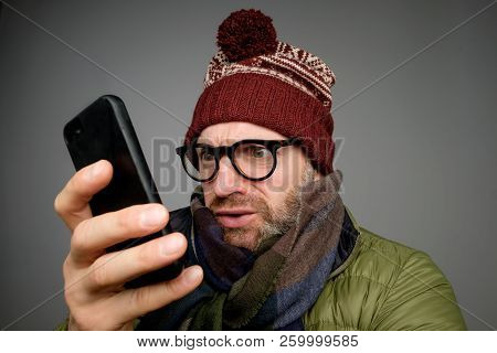 Funny Man In Glasses Anf Warm Clothes Typing Sms On Gray Background