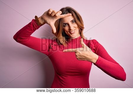 Young beautiful brunette woman wearing casual sweater stnding over pink background smiling making frame with hands and fingers with happy face. Creativity and photography concept.