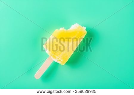 Yellow Popsicle With A Couple Of Bites On A Light Green Background