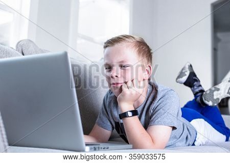 Cute young student doing online school work from home. Virtual Classroom or video conferencing from home. Connecting with teachers and fellow students while lying on the couch