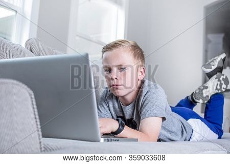 Cute young student doing online school work from home. Virtual Classroom or video conferencing from home. Connecting with teachers and fellow students while lying on the couch