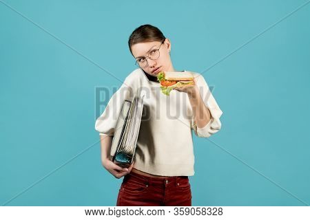 A Girl With Glasses With Documents Under Her Armpit Is Talking On The Phone And Is About To Eat A Sa