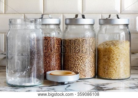 Full Glass Jars With Rice, Buckwheat, Barley And An Empty Sugar Jar On The Kitchen Table. Stock Duri
