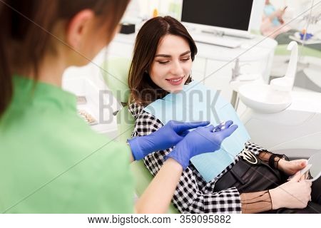 Dentist Shows Crown Samples To His Patient. Woman At The Dentist's Appointment Chooses The Tone Of V