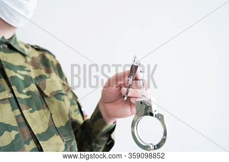 Police Officer With Face Mask And Handcuffs In Khaki Colored Uniform Stops, Arrest Criminal On The S