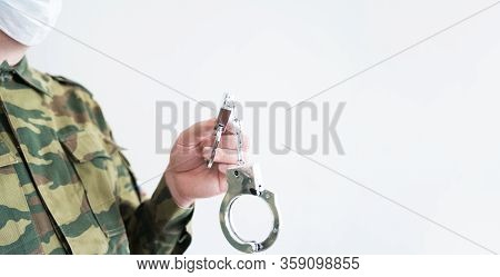 Police Officer With Face Mask And Handcuffs In Khaki Colored Uniform Stops, Arrest Criminal On The S