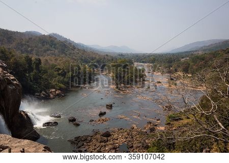 A Huge Waterfall Athirapally In Kerala, India. White Streams Of Water Of The Waterfall Break Into Sm