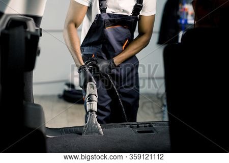 Professional Cleaning Of Car Interior By Wet Vacuum Machine. Clopped Image Of Male African Auto Serv