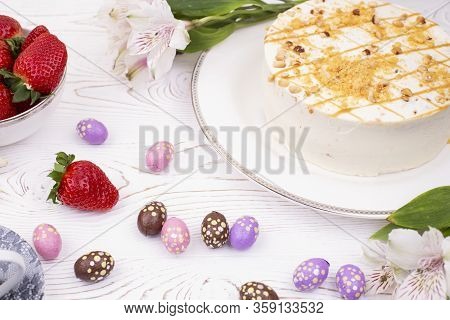 Cake Covered With White Cream And Nuts, Strawberries And Chocolate Eggs In A Multi-colored Falge.