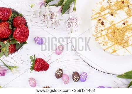 Cake Covered With White Cream And Nuts, Strawberries And Chocolate Eggs In A Multi-colored Falge.
