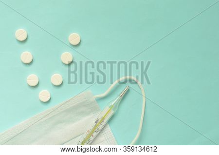 The Letter V In The Form Of Pills, Medical Mask And Termometer On Turquoise Background, Space For Te