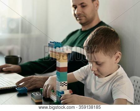 Four Year Old Boy Play With Building Set For Children And Dad Who Works At Aptop At Home. Home Worki