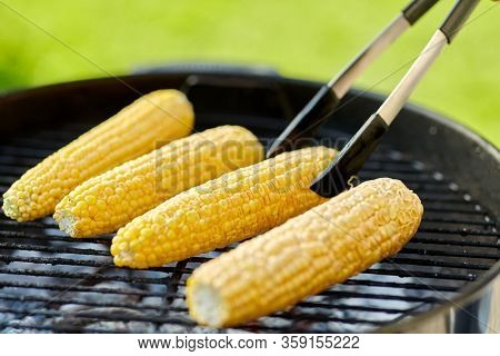cooking, barbecue and food concept - close up of corn roasting on brazier grill outdoors
