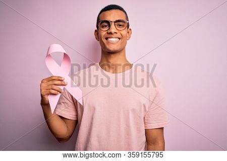 Young handsome african american man hoding pink cancer ribbon over isolated background with a happy face standing and smiling with a confident smile showing teeth