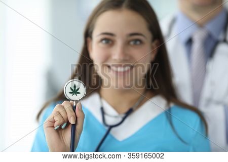 Close-up Of Female Hand Holding Stethoscope With Cannabis Symbol. Cheerful Smiling Nurse In Medical 