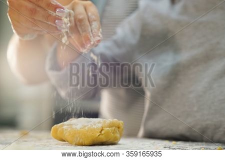 Hands of  kid and his mother sprinkle a piece of dough with flour, close up view.  Mother and child prepare food in the kitchen. Mother and son prepare dough for baking cookies.
