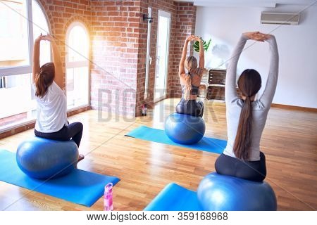 Young beautiful group of sportswomen practicing yoga. Stretching using fitness ball at gym
