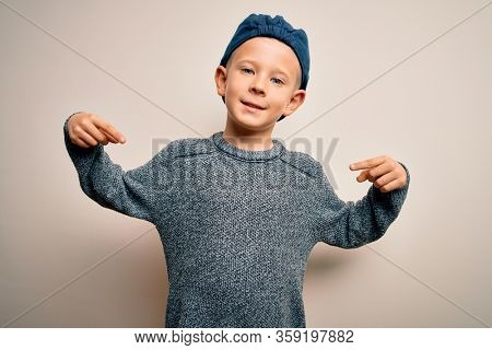 Young little caucasian kid with blue eyes wearing wool cap over isolated background looking confident with smile on face, pointing oneself with fingers proud and happy.