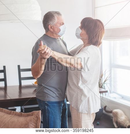 Coronavirus CoVid-19 Couple old aged senior people at home with seasona cold illness disease dancing. Elderly couple in medical masks during the pandemic