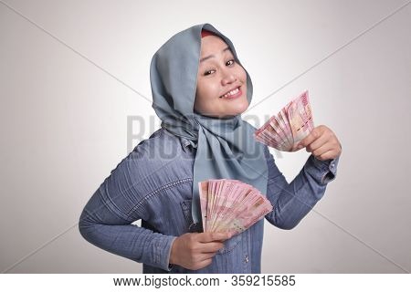 Portrait Of Indonesian Muslim Woman Holding Rupiah Money, Smiling Laughing Winning Gesture