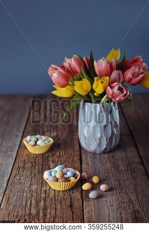 Easter Candies Covered Eggs In Various Pastel Colors In Paper Baskets Near Vase With Fresh Tulips On