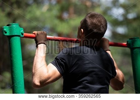 The Boy Pulls Himself Up On The Crossbar In The Park. Back View