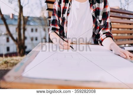 Girl In A Plaid Shirtis Engaged In Drawing While Sitting On A Benc