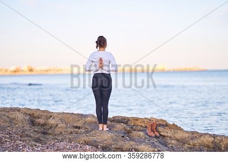 Young beautiful sportwoman practicing yoga. Coach standing on backview teaching revers prayer pose at the beach