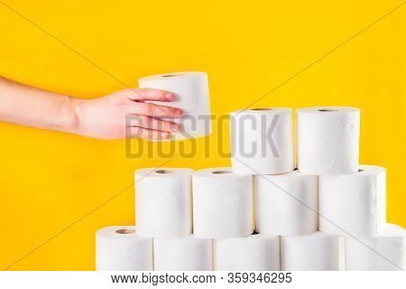 Close Up Caucasian Male Hand Takes A Roll Of Toilet Paper From A Folded Tower Of Rolls On Bright Yel