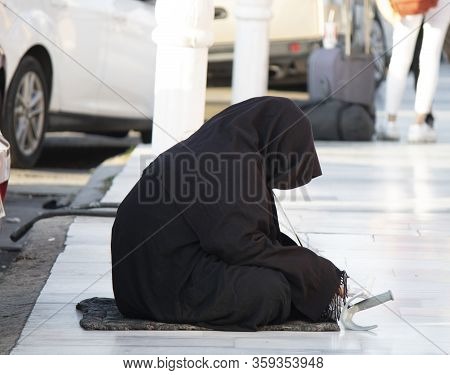 Woman Dressed In Black Burka Is Begging On Marble Parquet.