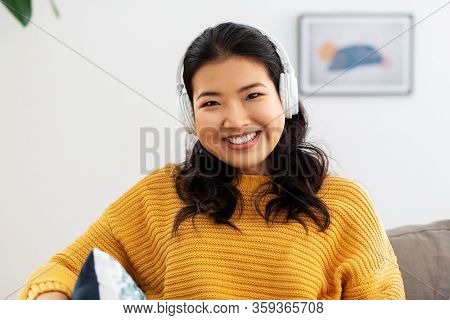 people and leisure concept - happy smiling asian young woman in headphones listening to music at home
