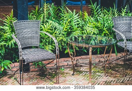 A Vintage Metal Table And 2 Chairs Are On The Outside Of The Coffee Shop, With Ferns And Glass Wall 