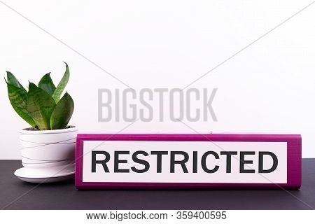 Folder With The Text Label Restricted Lies On A Dark Table With A Flower And A Light Background.