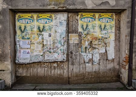Manzano, Italy - 25.03.2020: Cityscape. View Of Old Wooden Gate Used As A Bulletin Board: Old Poster