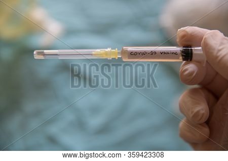 Close Up Shot Of A Syringe With The Word Coronavirus Vaccine.he Is Holding Her Hand With A White Lat