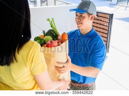 Wfh: Food Delivery Service Man In Blue Uniform. Thai Deliveryman Holding Fresh Food For Young Woman.