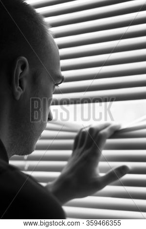 A Young Man Look Out The Window Throgh The Blinds Soft Focus