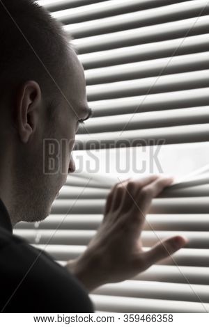 A Young Man Look Out The Window Throgh The Blinds Soft Focus