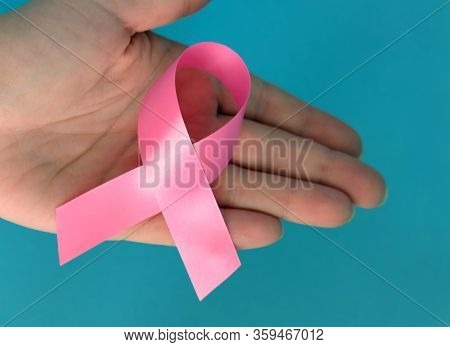 Pink Ribbon On A Womans Handon And Blue Background. Breast Cancer Concept Symbolic Tape