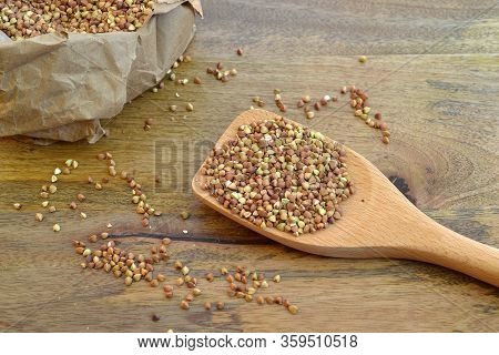 Buckwheat Groats In Larege Wooden Spoon And In Paperbag, On Wood Background,  Viewed From Above- Hea