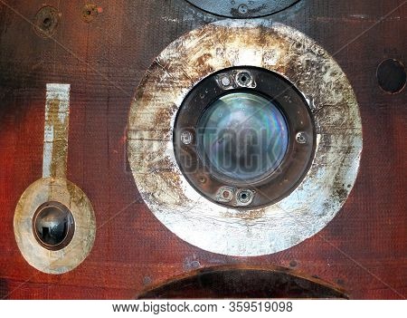 A Close Up Of A Round Porthole On A Used Russian Space Re-entry Vehicle With Burned Red And Black St