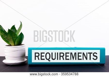 Folder With The Label Requirements Lies On A Dark Table With A Flower And A Light Background