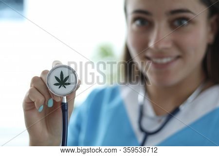 Close-up Of Female Hand Holding Stethoscope With Cannabis Sign. Smiling Doctor Practitioner In Medic