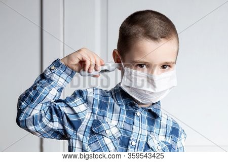 Young Boy With Sore Eyes In A Medical Mask Measures The Temperature Of A Thermometer In His Ear. Med