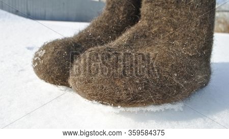 Brown Felt Boots Close-up. Snow Stuck To The Boots. Valenoks Are Covered With Small Ice Floes.
