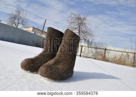 Brown Felt Boots. Snow Stuck To The Boots. Valenoks Are Covered With Small Ice Floes. The Shadow Of 